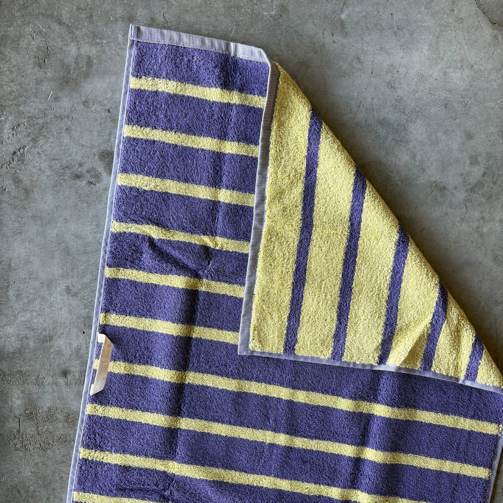 Folded towel with purple and yellow stripes on a concrete surface