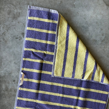 Folded towel with purple and yellow stripes on a concrete surface