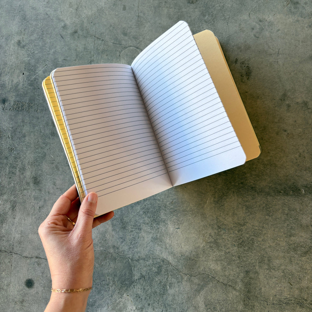 Open notebook held by a hand on a concrete floor